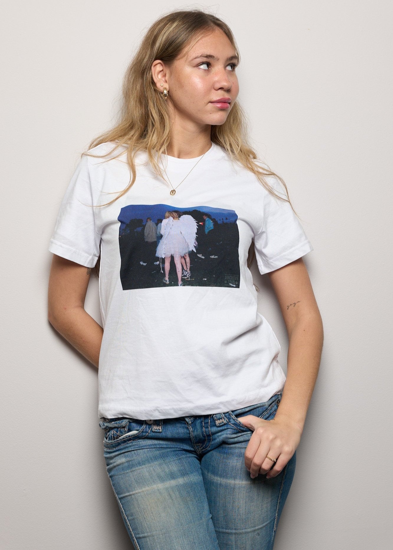 Model wearing Archive Tees women's t-shirt in white with a vintage picture of a girl wearing angel wings at dawn at the Creamfields dance music festival in 1998. Vintage music festival T-shirt.