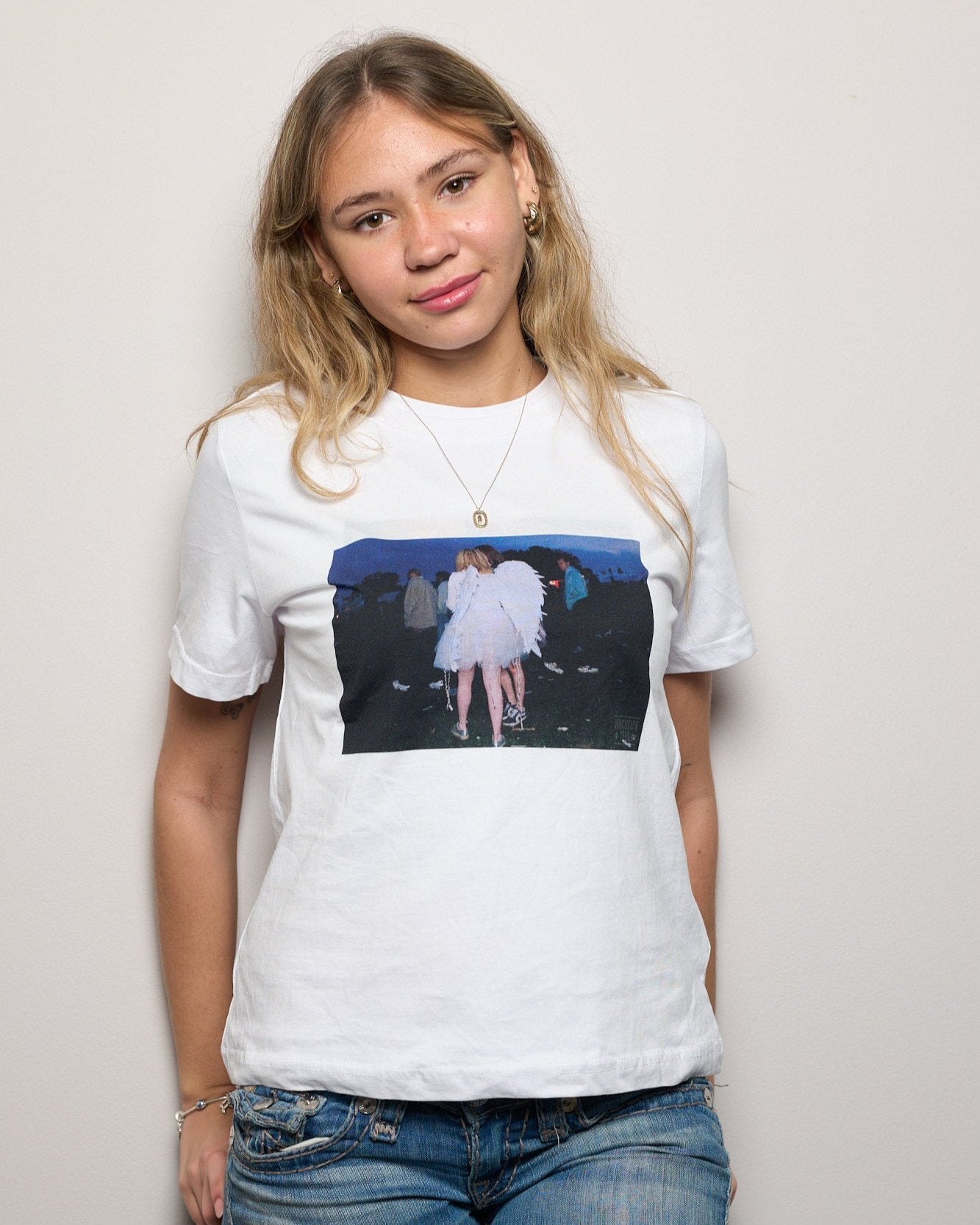 Model wearing women's t-shirt in white with a vintage picture of a girl wearing angel wings at dawn at the Creamfields dance music festival in 1998 by Archive Tees. Vintage music festival T-shirt.